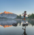 woman in hiking clothes hopping across stones in a mountainside lake